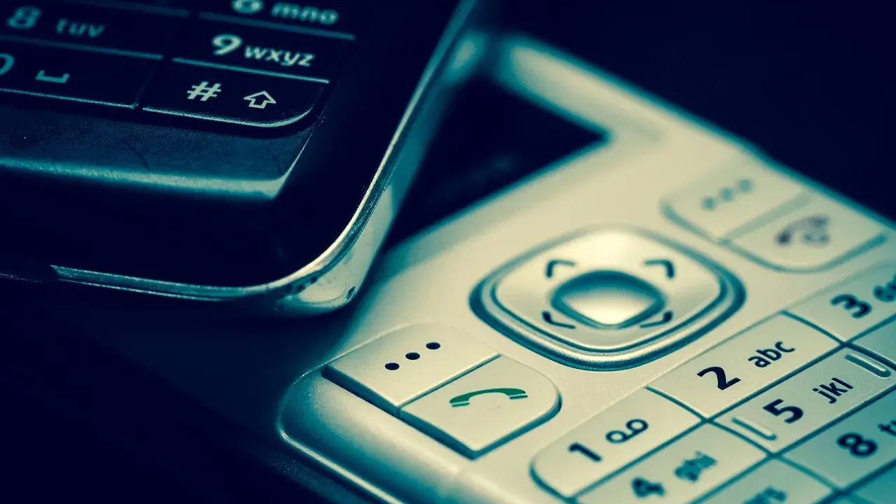 Zbliżenie na klawiatury dwóch telefonów komórkowych, jeden czarny, drugi srebrny.