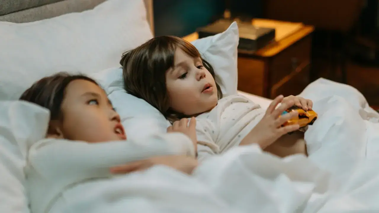 Dos niños en la cama, uno con un coche de juguete, quizás planeando travesuras o contando mentiras en niños de 10 a 12 años.