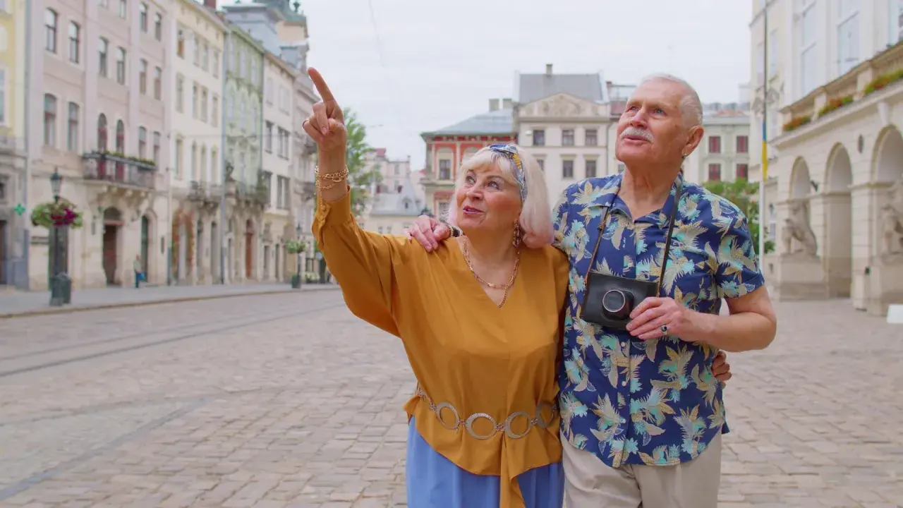 Starsze małżeństwo odkrywa urokliwe, przyjazne seniorom miasta. Kobieta z aparatem wskazuje na zabytkową architekturę.