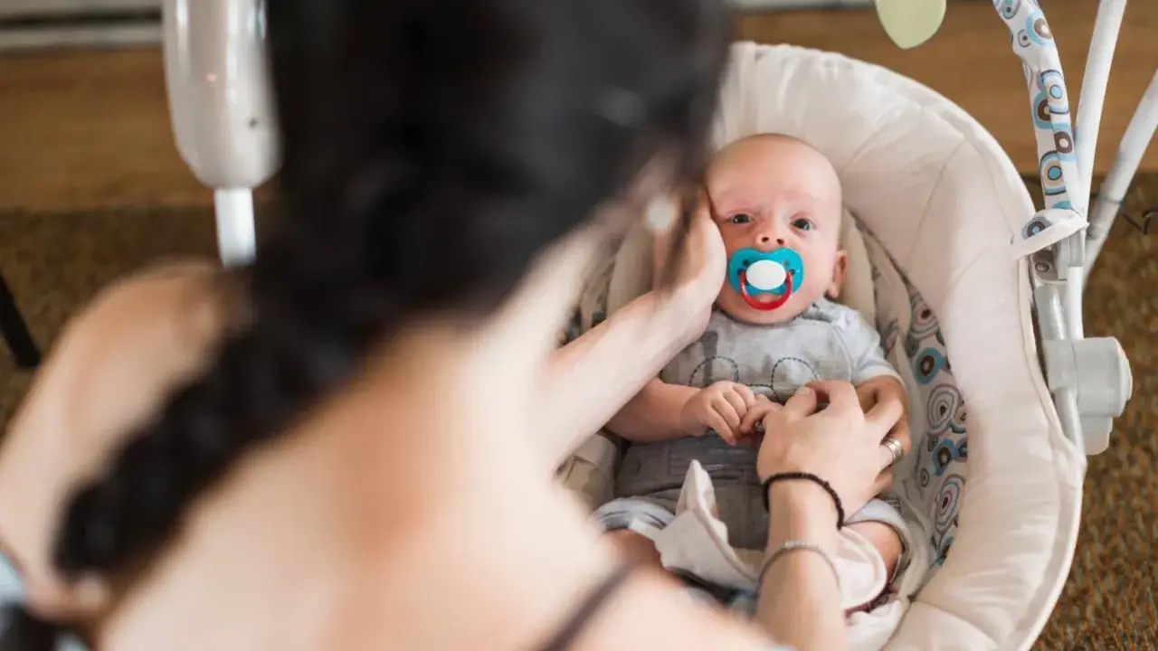 Maluszek w bujaczku polecanym przez fizjoterapeutów. Mama delikatnie głaszcze go po główce, uspokajając.