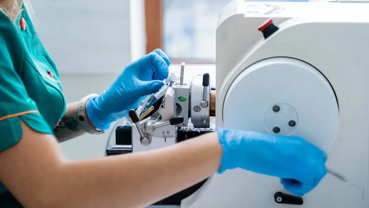 Laborantka w niebieskich rękawiczkach pracuje przy mikrotomie. Czy biopsja jest bezpieczna? Tak, dzięki precyzyjnym narzędziom i doświadczeniu.