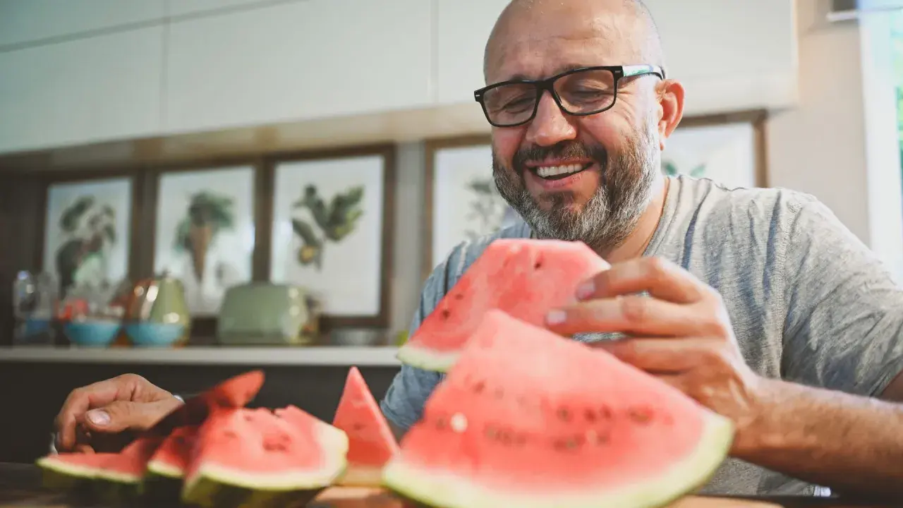Glücklicher Mann mit Brille isst Wassermelone. Die Wassermelone Nachteile sind, dass sie schnell aufgebraucht ist.