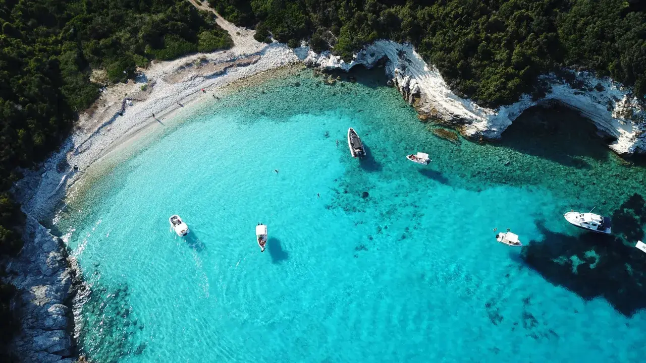 Idealne wakacje na Paxos: turkusowa woda, białe skały i łodzie unoszące się na falach.