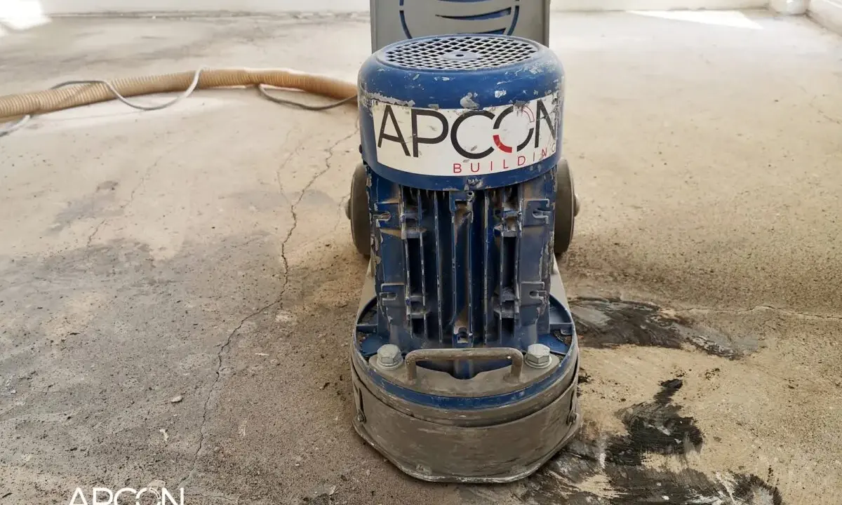 Maszyna APCON przygotowuje podłoże pod parkiet, szlifując beton. Wąż odkurzacza leży obok.