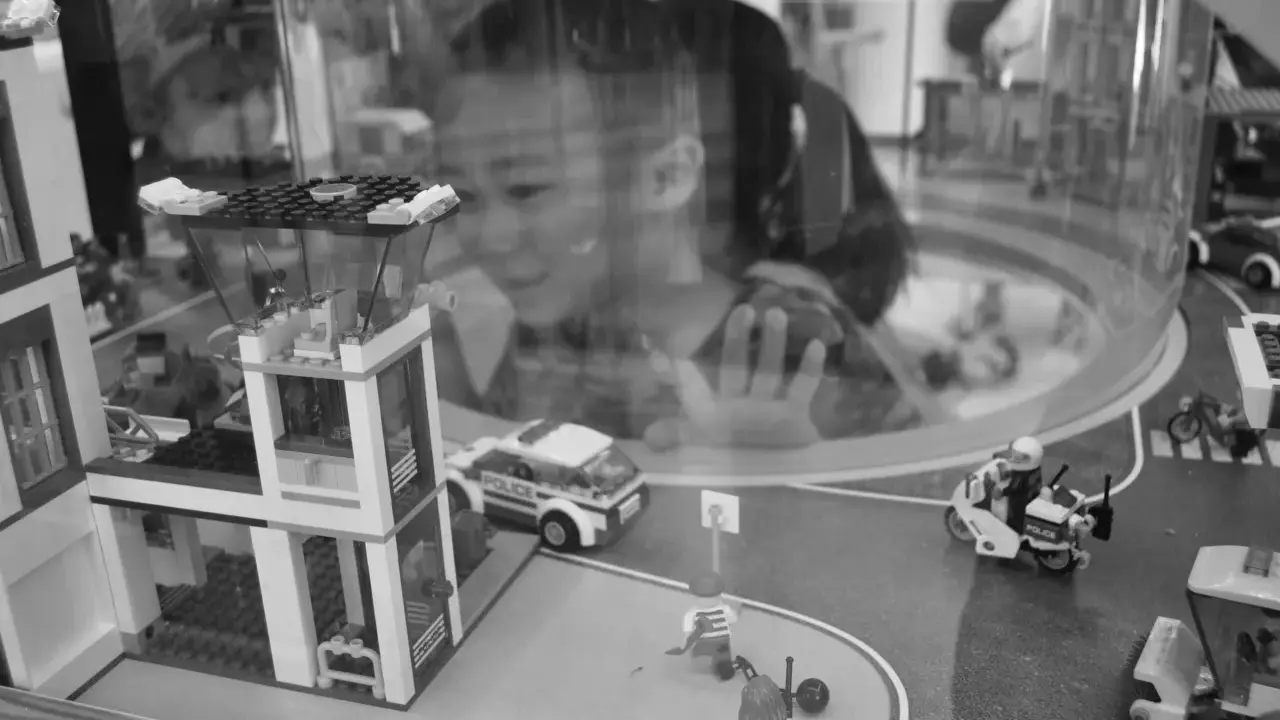 Bambina osserva con stupore un **reportage fotografico** di idee con costruzioni Lego: un commissariato, auto della polizia e personaggi in azione.