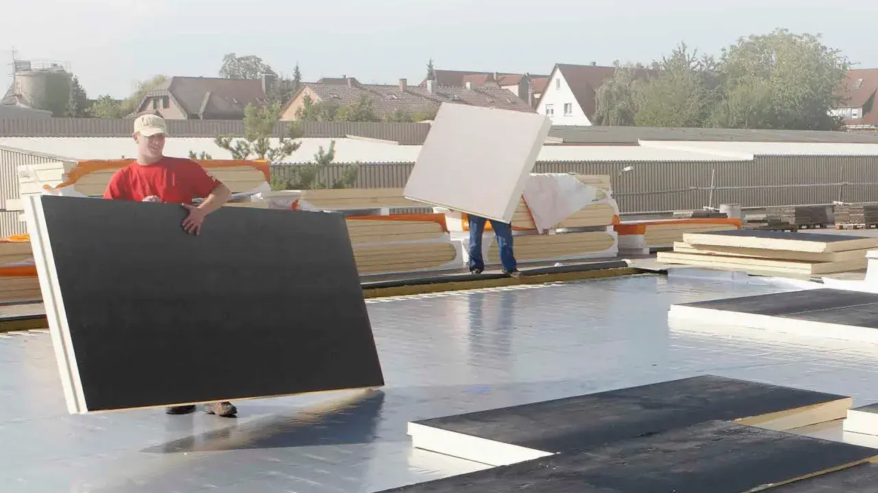 Arbeiter verlegen Dämmplatten auf einem Dach. Die Platten entsprechen der DIN 18234 und werden für die Dachisolierung verwendet.