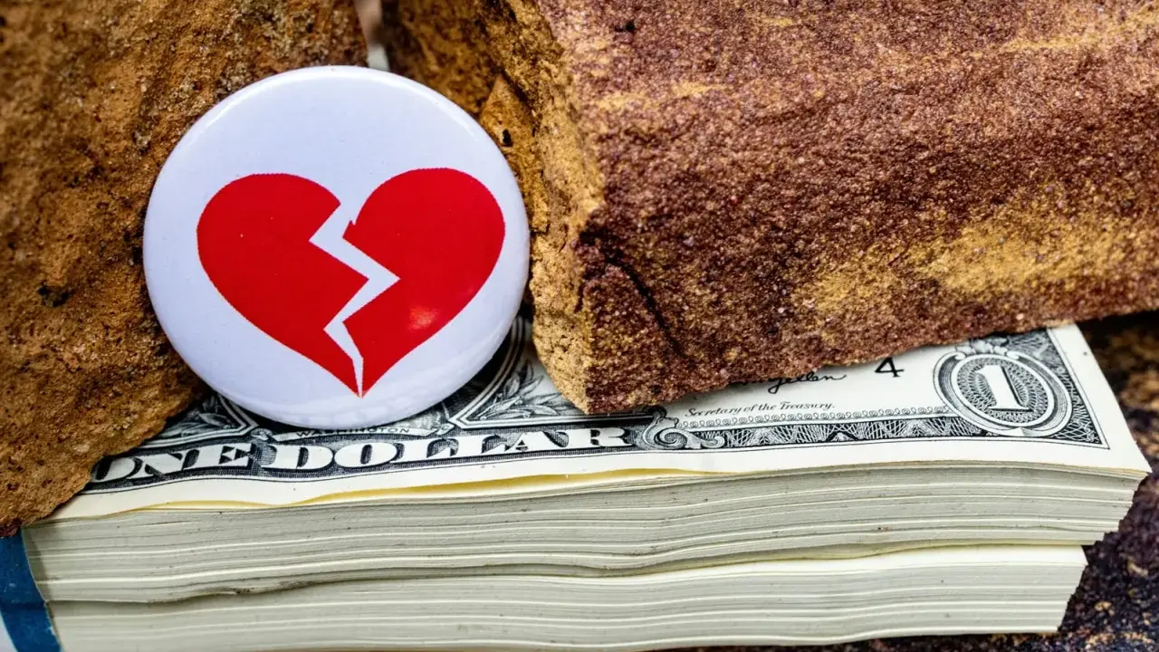 Symbol złamanego serca na stosie dolarów, między kamieniami. Nieoficjalna separacja, gdzie pieniądze dzielą.
