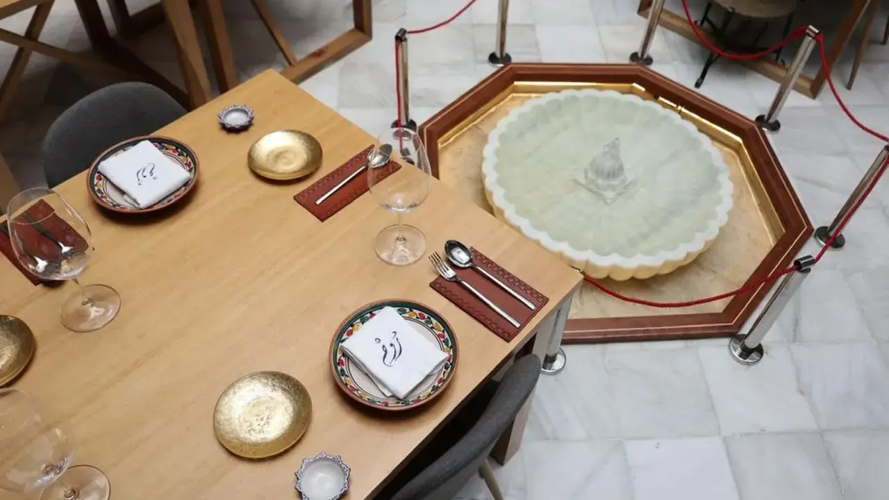 Mesa elegante en el restaurante El Puente El Tejar, con vajilla dorada y una fuente ornamental en el centro.