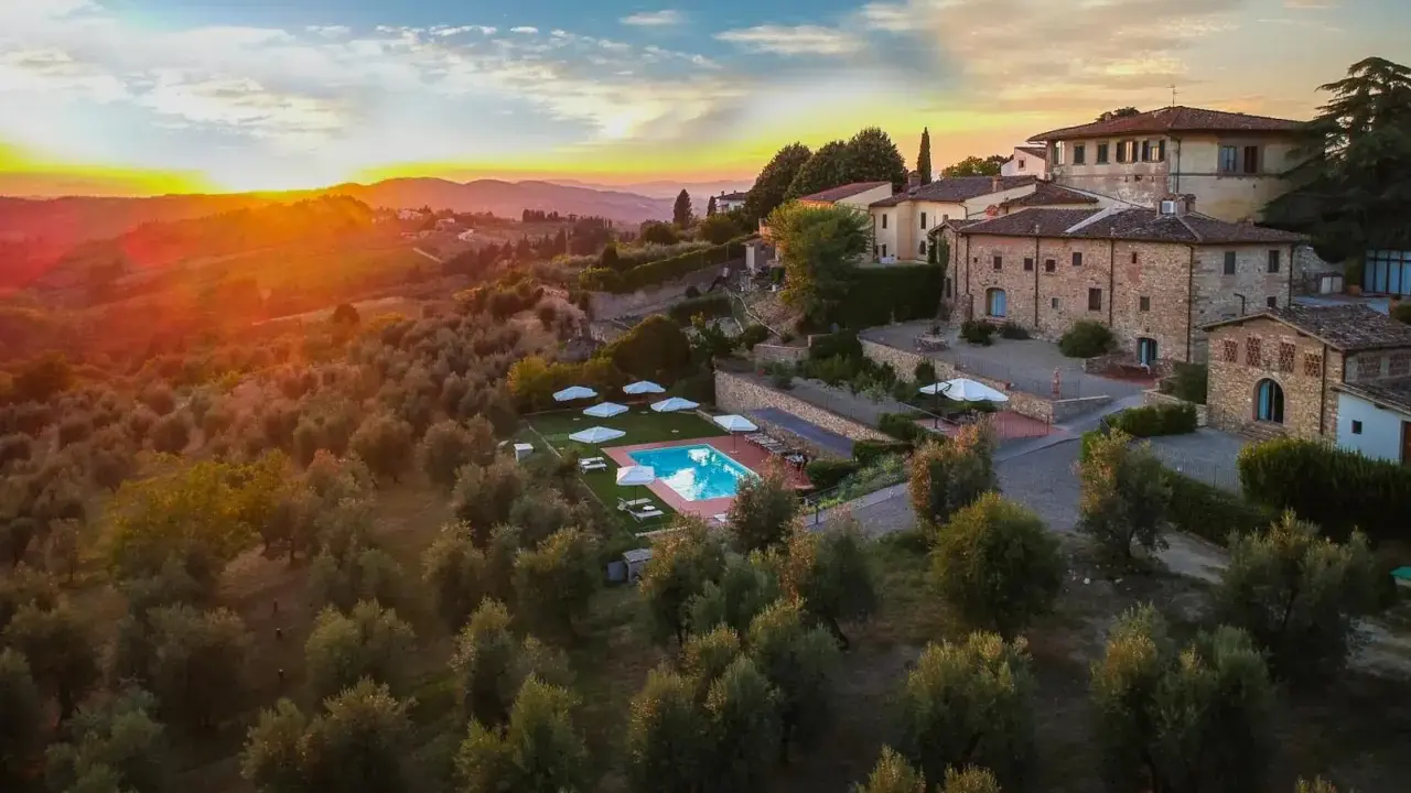 Un tramonto dorato illumina un agriturismo con piscina, immerso tra ulivi e colline, perfetto per un tour della Toscana.
