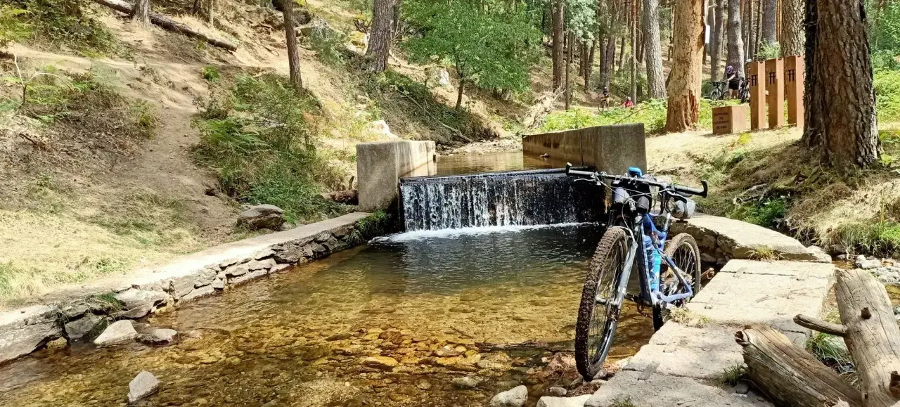 Bicicleta de montaña junto a una cascada en un arroyo, ideal para rutas por Segovia.