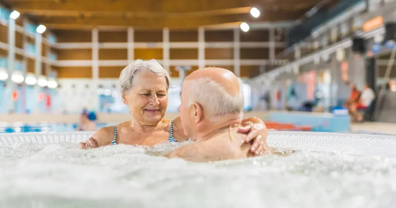 Uśmiechnięta para seniorów relaksuje się w jacuzzi w basenie. To wspaniałe miejsce, jak sanatorium szpitalne, gdzie można odzyskać siły.