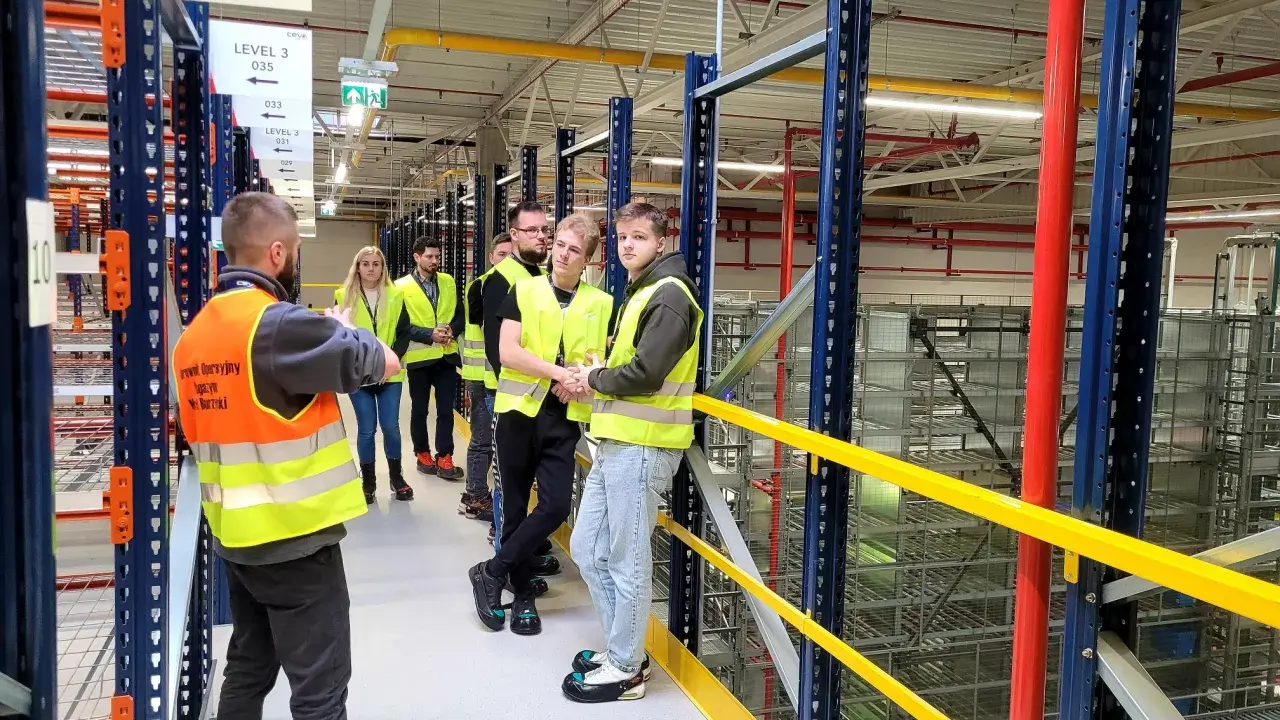 Grupa osób w kamizelkach odblaskowych zwiedza magazyn CEVA Logistics. To potencjalna ceva logistics praca.