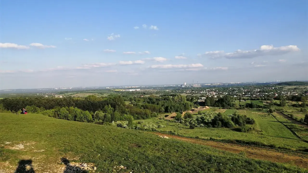 Widok z góry Siewierskiej na zielone pola i lasy, w oddali widać zabudowania i kominy.