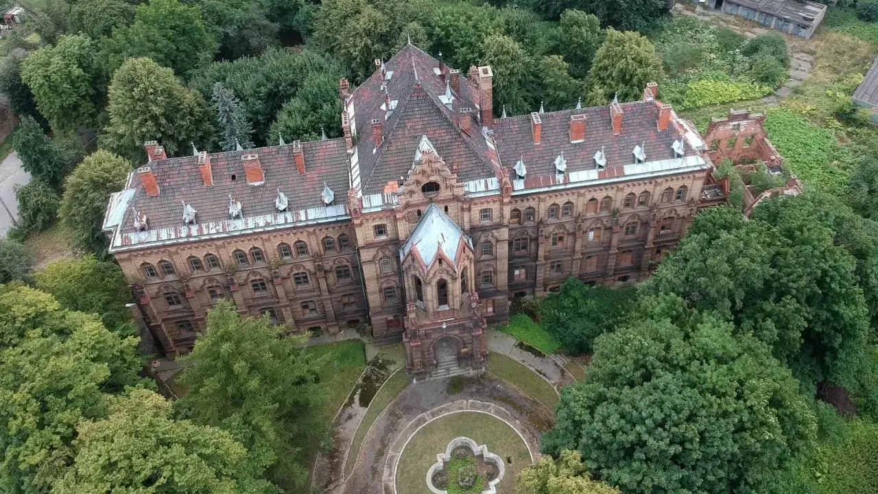 Mokrzeszów pałac, rozległy, ceglany budynek z charakterystycznym dachem, otoczony bujną zielenią.