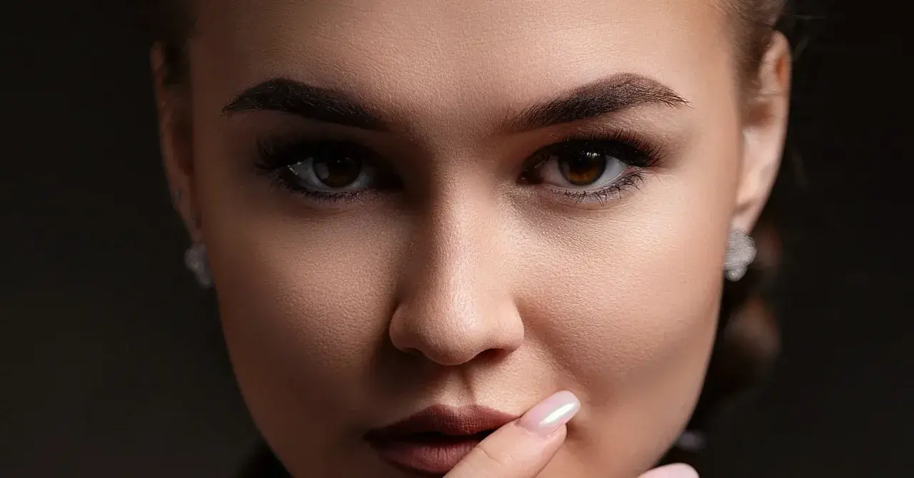 Gros plan sur un visage féminin aux **sourcils droits** et maquillés. Elle porte des boucles d'oreilles discrètes.