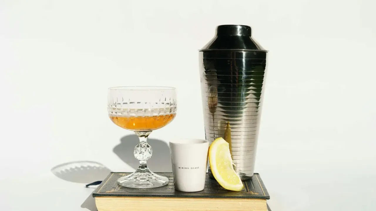 Szklanka z drinkiem, shaker, cytryna i książka. Idealne akcesoria, by dowiedzieć się, z czym pić amarula.