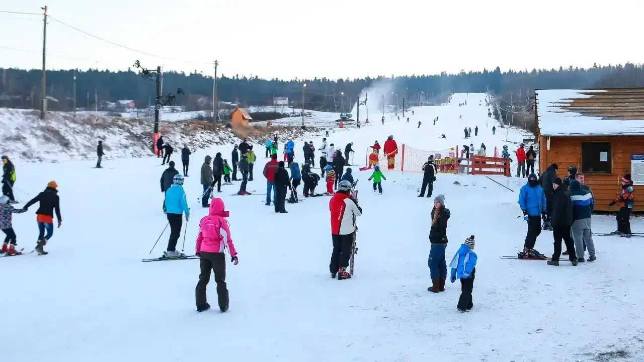 Ludzie jeżdżą na nartach i snowboardach, ciesząc się zimowymi atrakcjami. Warunki na stokach wydają się dobre, śnieg jest obecny, a pogoda sprzyja aktywnościom na świeżym powietrzu.