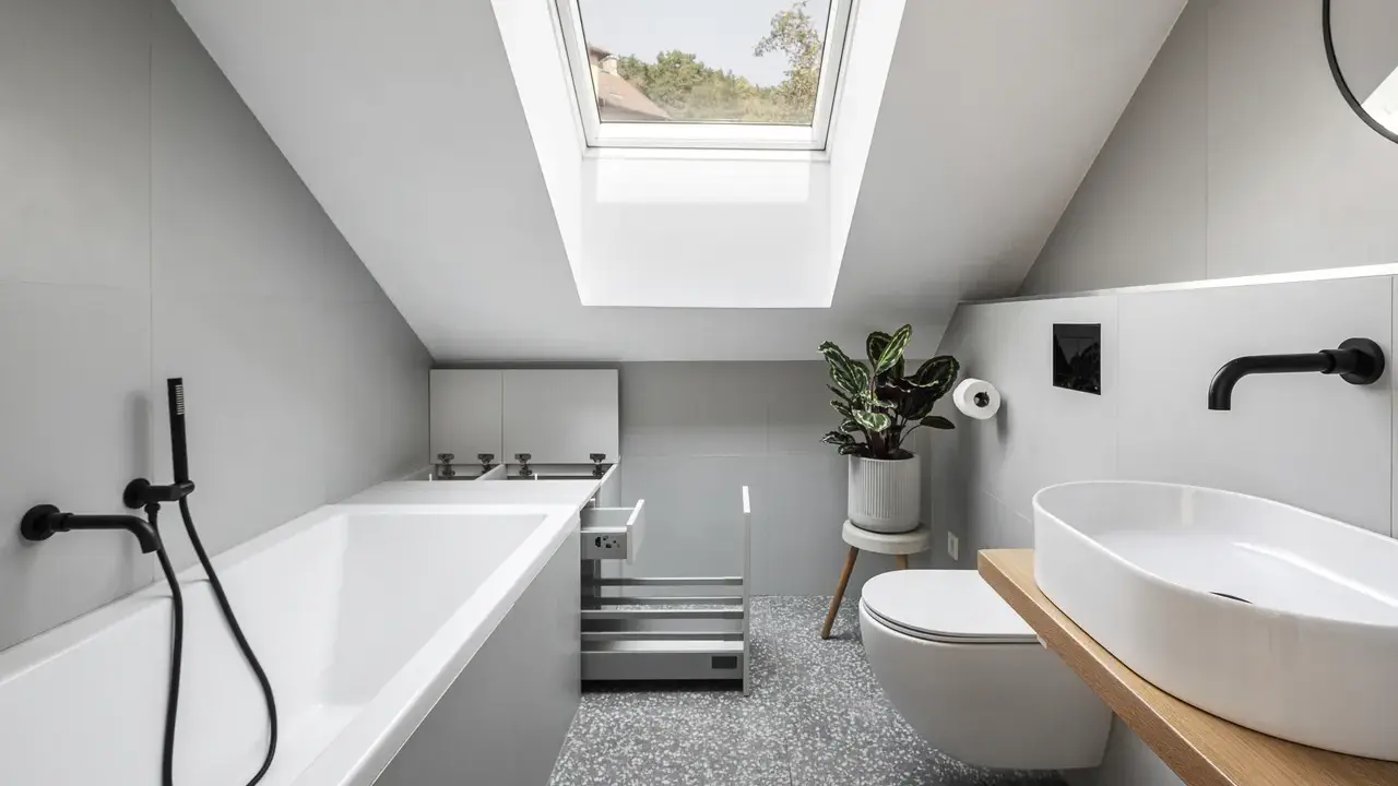 Un piccolo bagno sottotetto basso con vasca, WC, lavabo e lucernario.