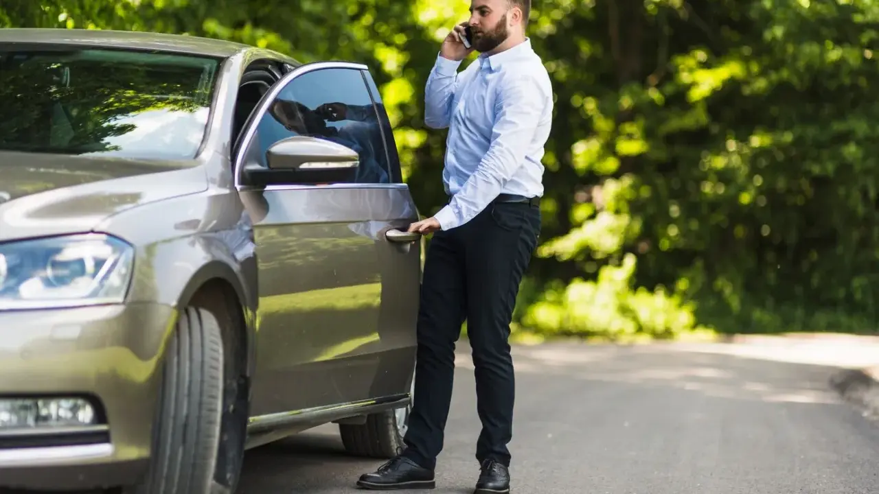 Mężczyzna rozmawia przez telefon, stojąc przy otwartych drzwiach swojego samochodu. Wygląda, jakby potrzebował pomocy, a nie jakby zostawił porzucone samochody.