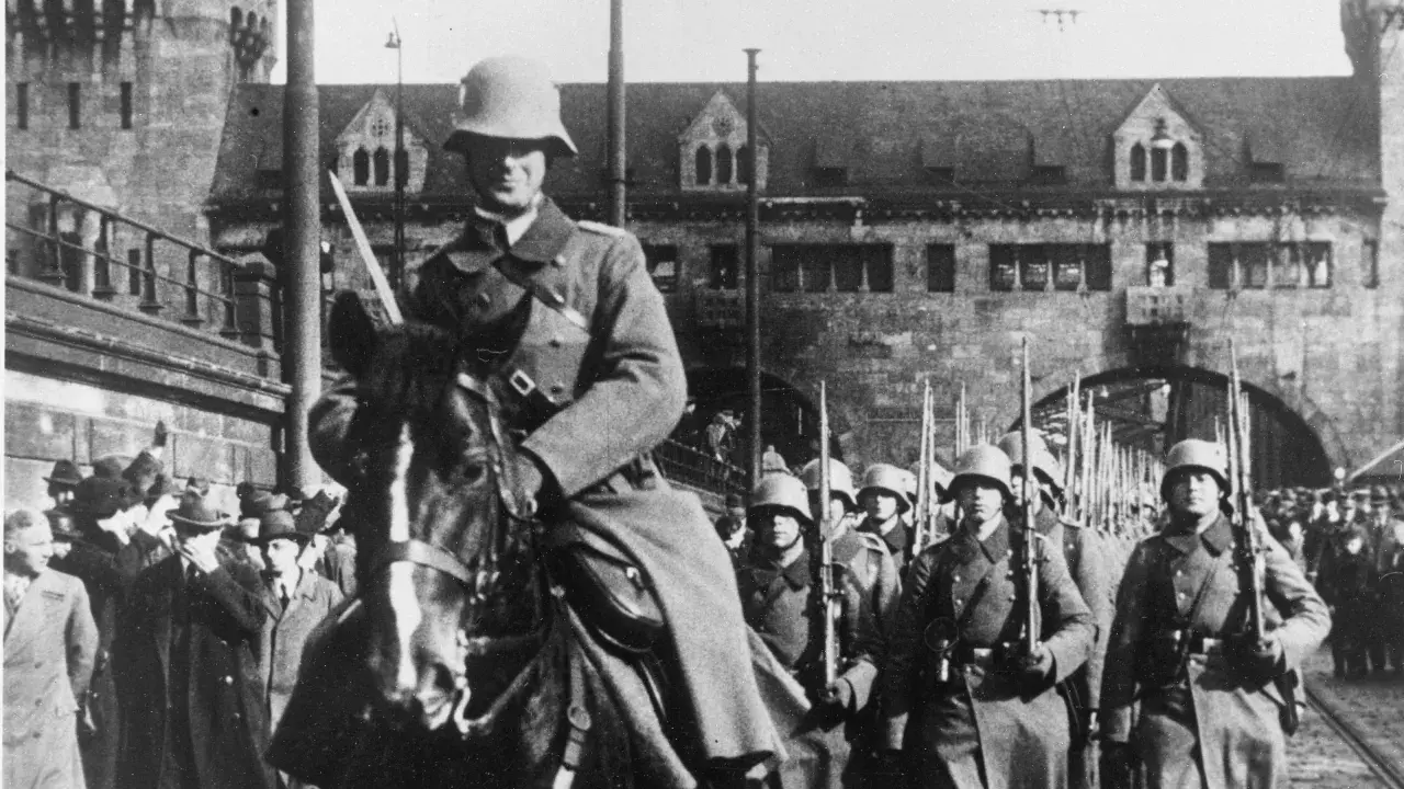 Soldaten marschieren in Formation, ein Reiter führt sie an. Ein historisches Bild der Rheinlandbesetzung 1936.