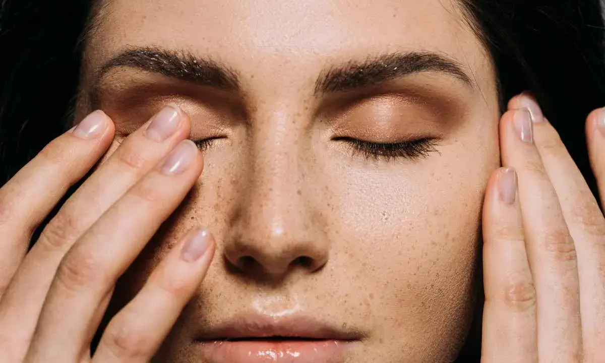 Primo piano di una donna con lentiggini, che si tocca il viso. Potrebbe indicare sintomi di carenza vitamina d sulla pelle.