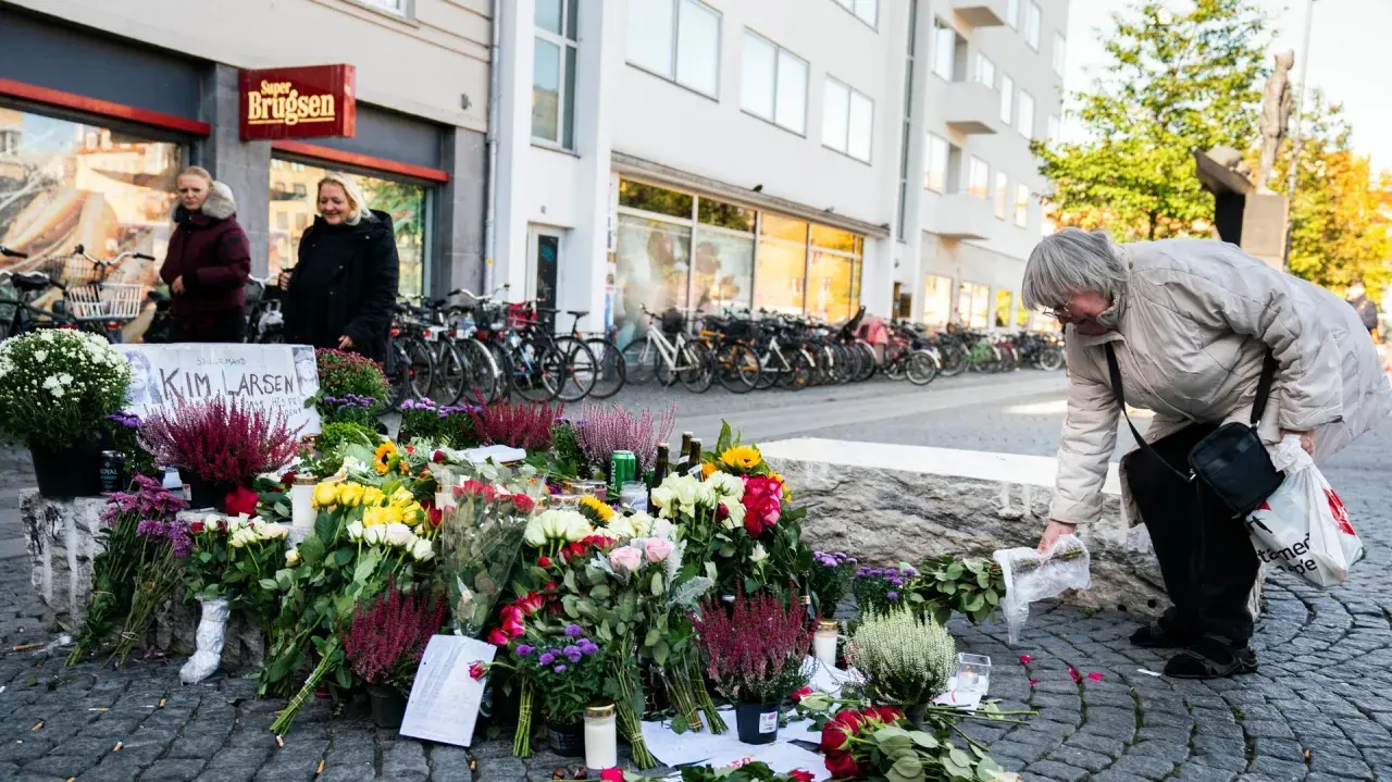 En kvinna lägger blommor vid en minnesplats för Kim Larsen. Många blommor och ljus.