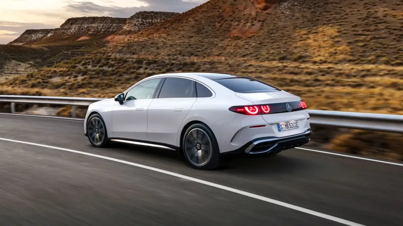 Weißer Mercedes C-Klasse EQ fährt auf einer Straße in bergiger Landschaft.