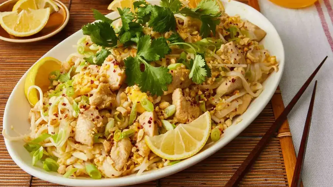 Pyszne pad thai co to? Danie z kurczakiem, makaronem ryżowym, orzeszkami ziemnymi i świeżą kolendrą, podane z cytryną.
