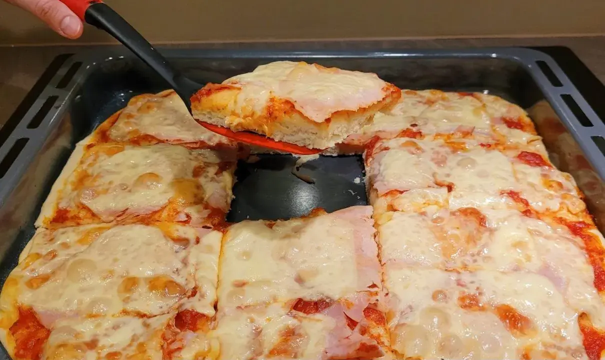 Ania gotuje pizzę. Gorąca, domowa pizza z serem i szynką, właśnie wyjęta z blachy.