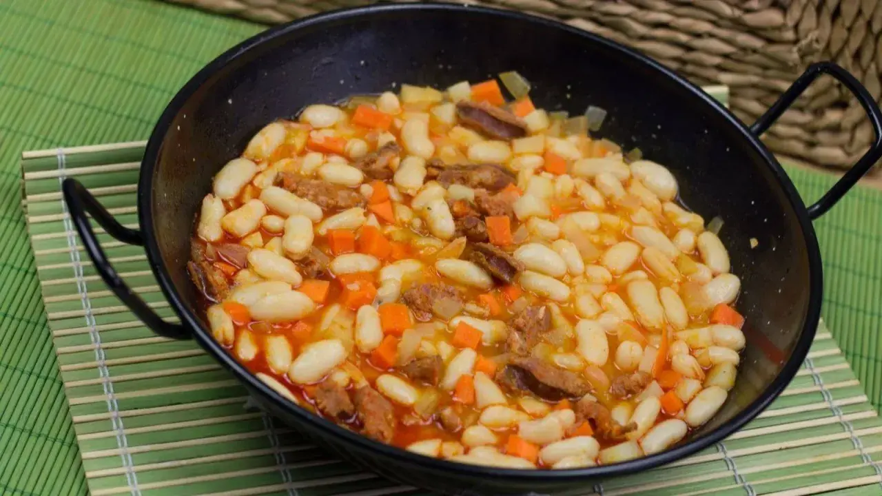 Alubias con chorizo y verduras en una paellera, plato tradicional español.