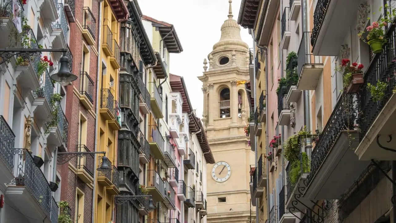 Edificio con balcónes floridos y torre de iglesia en Navarra. ¿Buscas ayudas cambio ventanas Navarra?