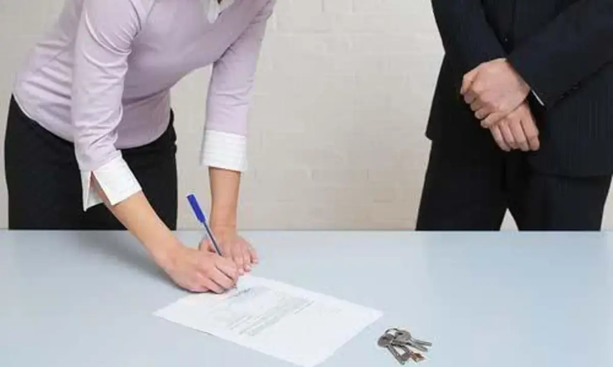 Une femme signe un document, peut-être un passage expert assurance habitation, tandis que des clés reposent sur la table.