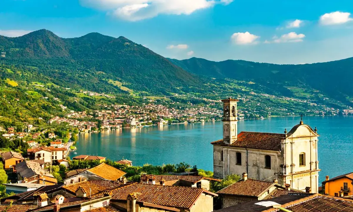 Un borgo pittoresco sul lago, ideale per gite in giornata da Milano. Case con tetti rossi, una chiesa e montagne verdi sullo sfondo.