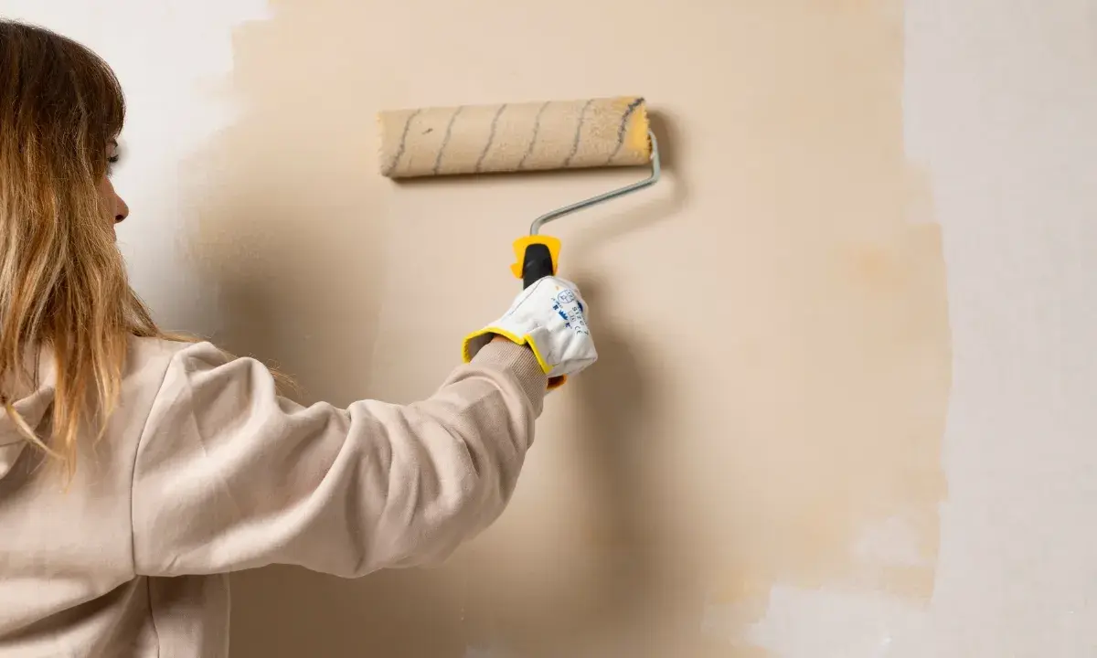 Persona aplicando pintura con rodillo, un truco para pintar sin cinta de carrocero y lograr bordes perfectos.