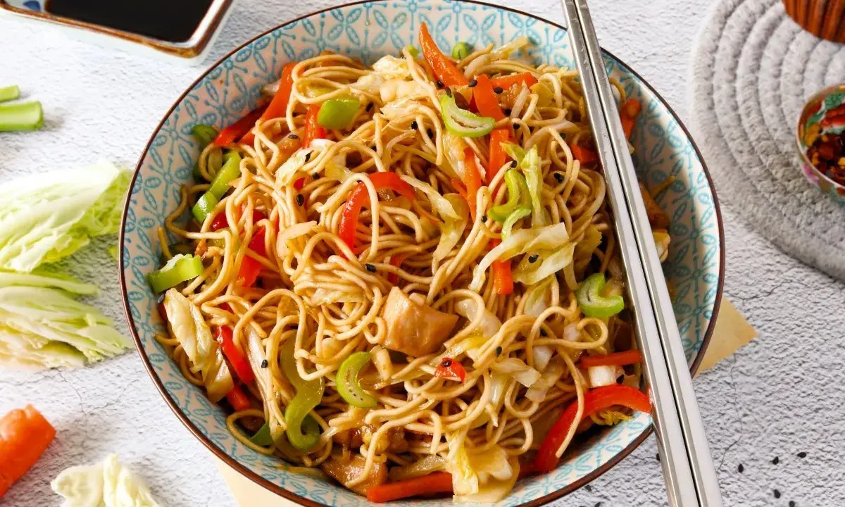 Un plato de chow mein con verduras coloridas y palillos listos para disfrutar.