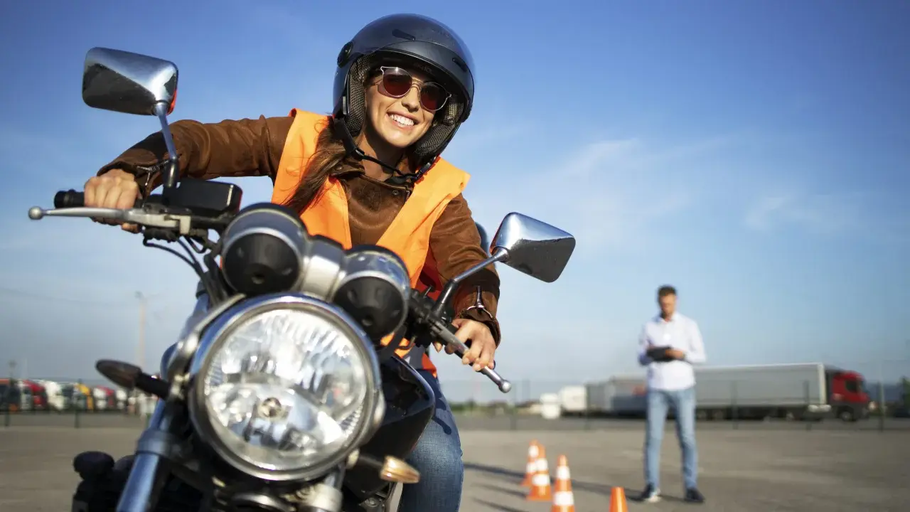 Mujer sonriente con casco y chaleco naranja, lista para obtener su carnet AM B en una autoescuela.