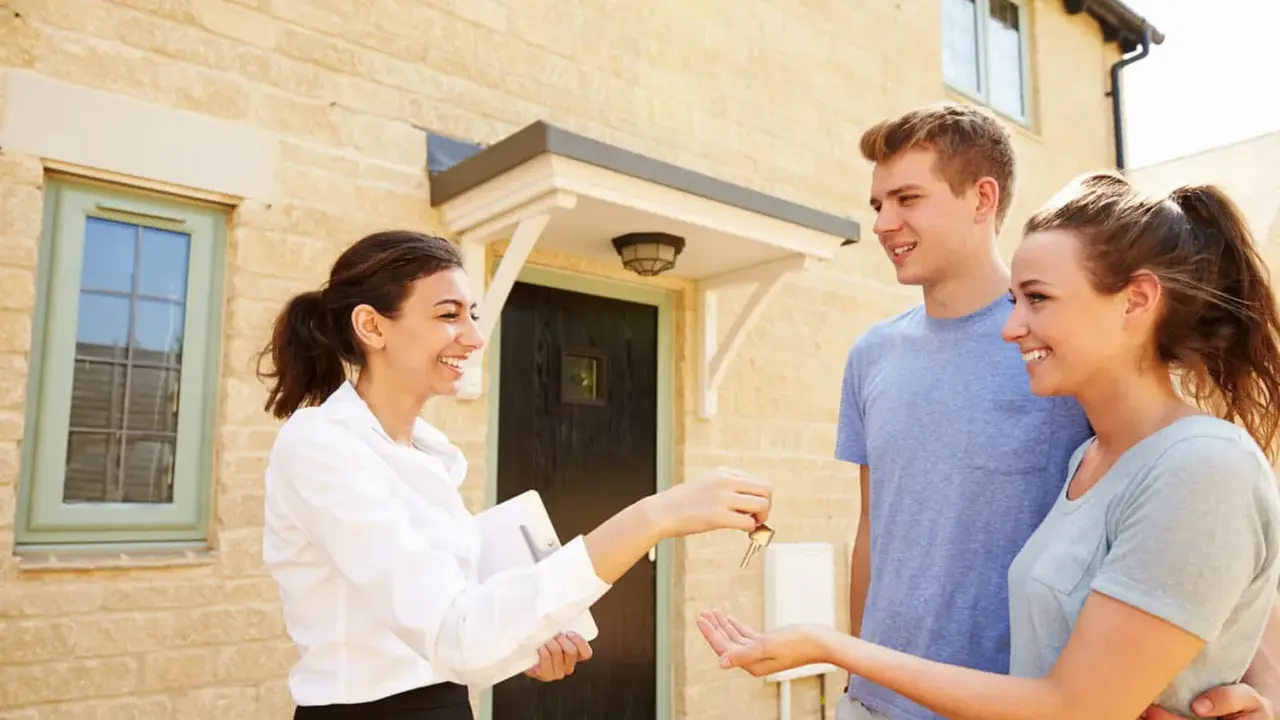 Une agent immobilier remet les clés d'une maison à un jeune couple. Ils sont heureux d'acquérir leur nouveau logement, peut-être grâce au droit de préemption locataire.