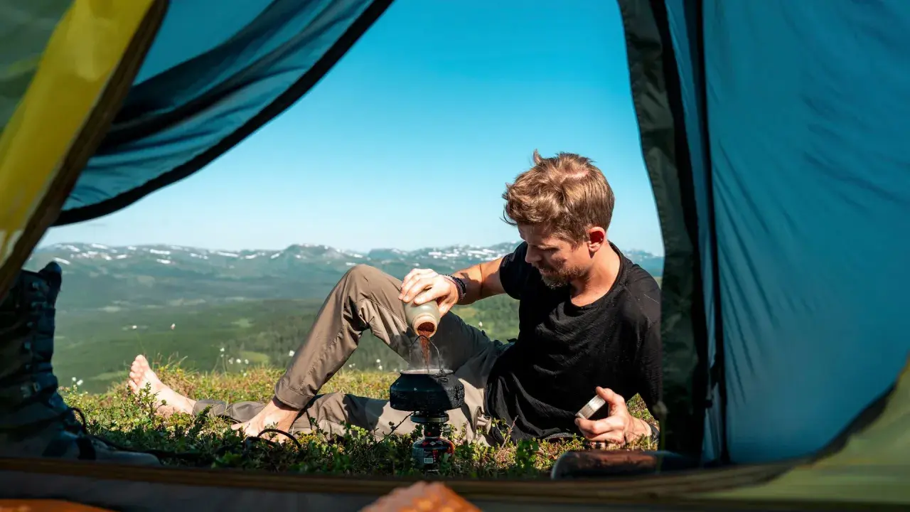 Man förbereder kaffe utanför tältet med en fantastisk utsikt. En del av packlista vandring sommar.