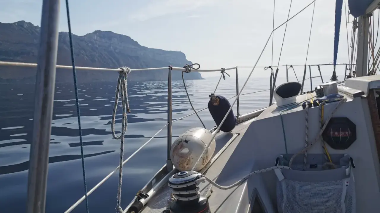 Vue depuis un voilier Aquila, naviguant sur une mer calme avec des falaises en arrière-plan. Avis de navigation paisible.