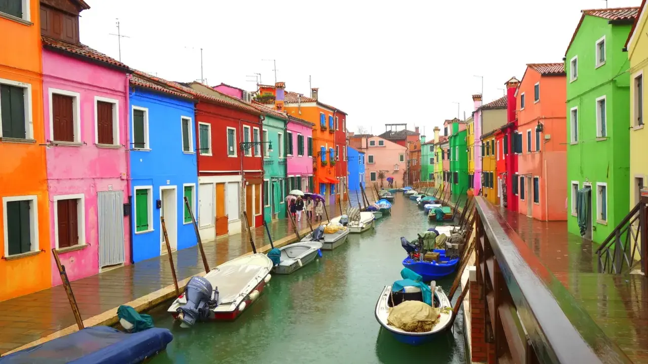Venise : une maison colorée et d'autres maisons aux teintes vives bordent un canal où flottent des bateaux.