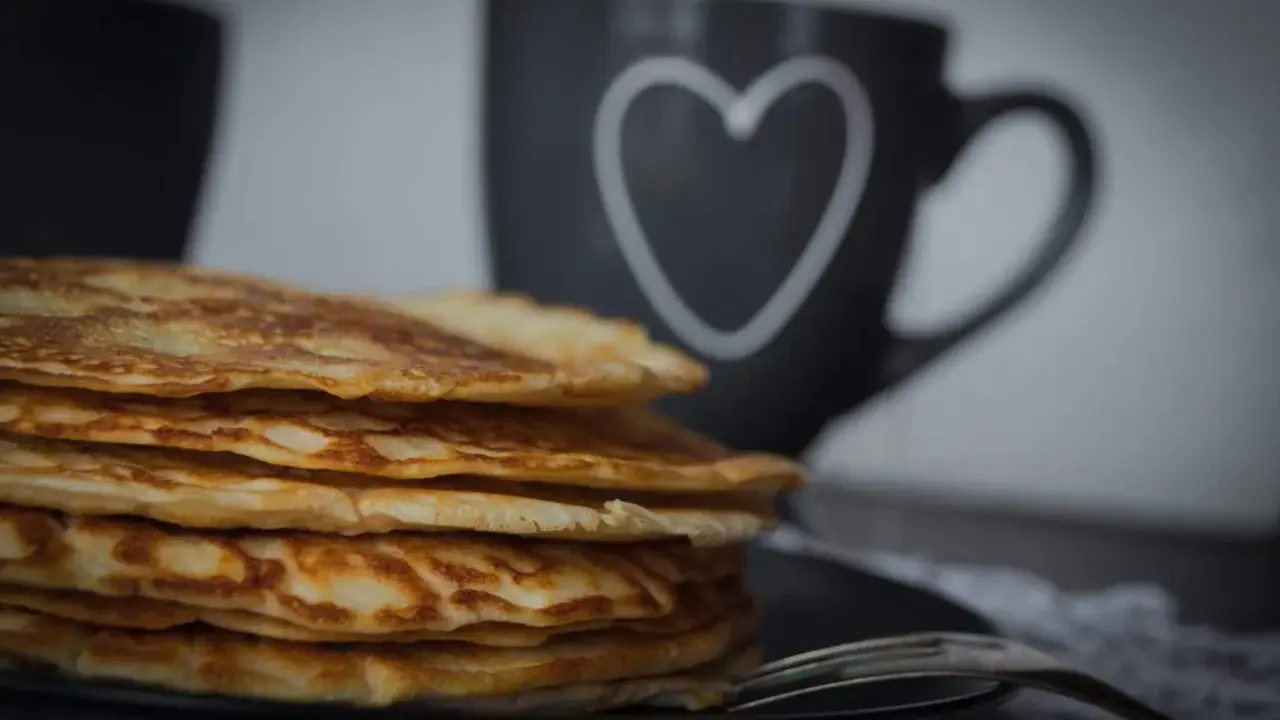 Stapel goldbrauner, **high protein pancakes** auf schwarzem Teller, daneben eine Tasse mit Herz.