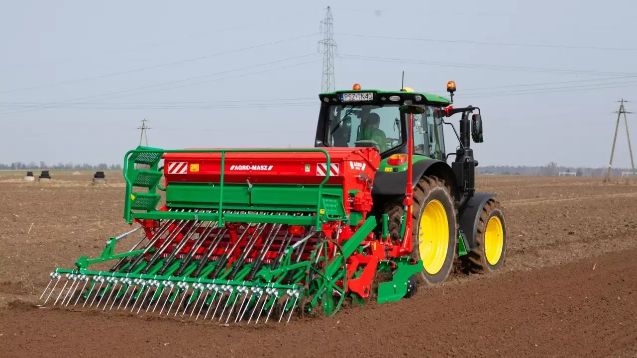 Zielony traktor z siewnikiem Agro-Masz pracuje na polu. Maszyna precyzyjnie wysiewa nasiona, optymalizując ile trawy na hektar zostanie zasiane.
