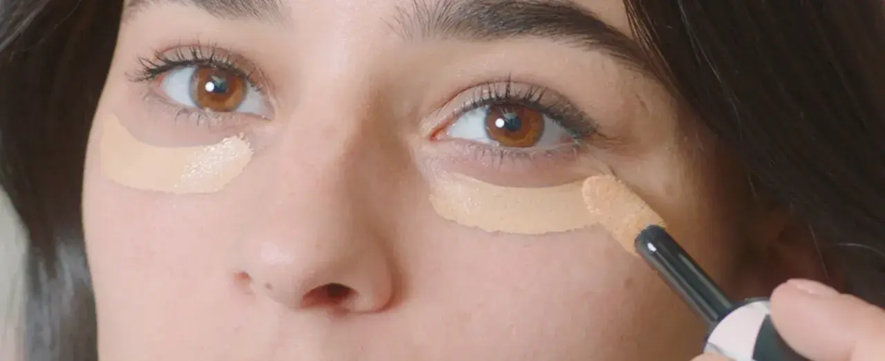 Aplicando corrector para disimular las ojeras antes o después del maquillaje.