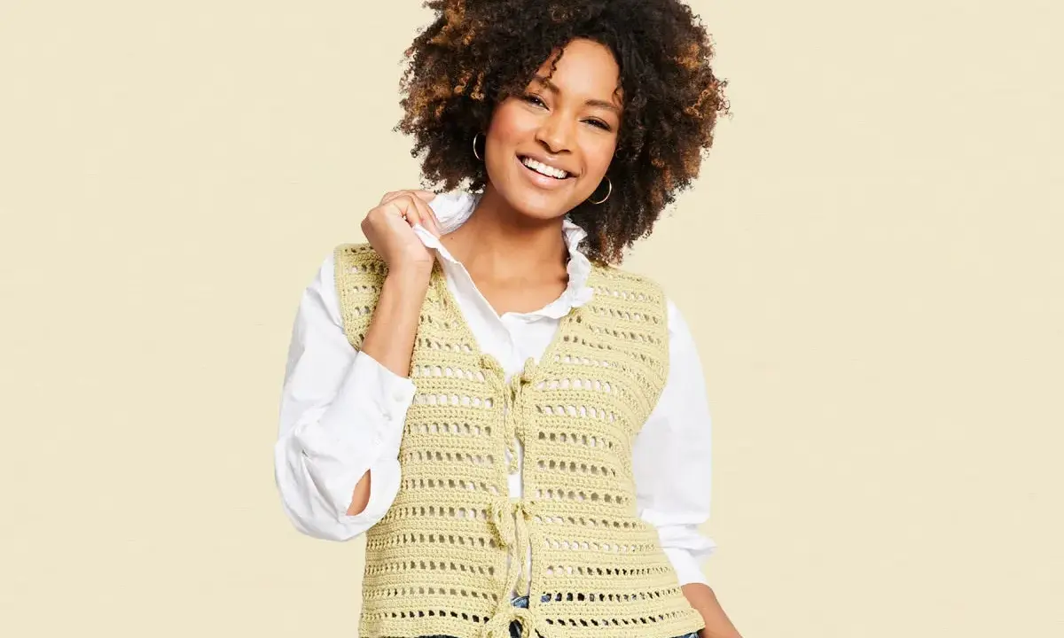 Mujer sonriente con chaleco de crochet con patrón calado, atado al frente.