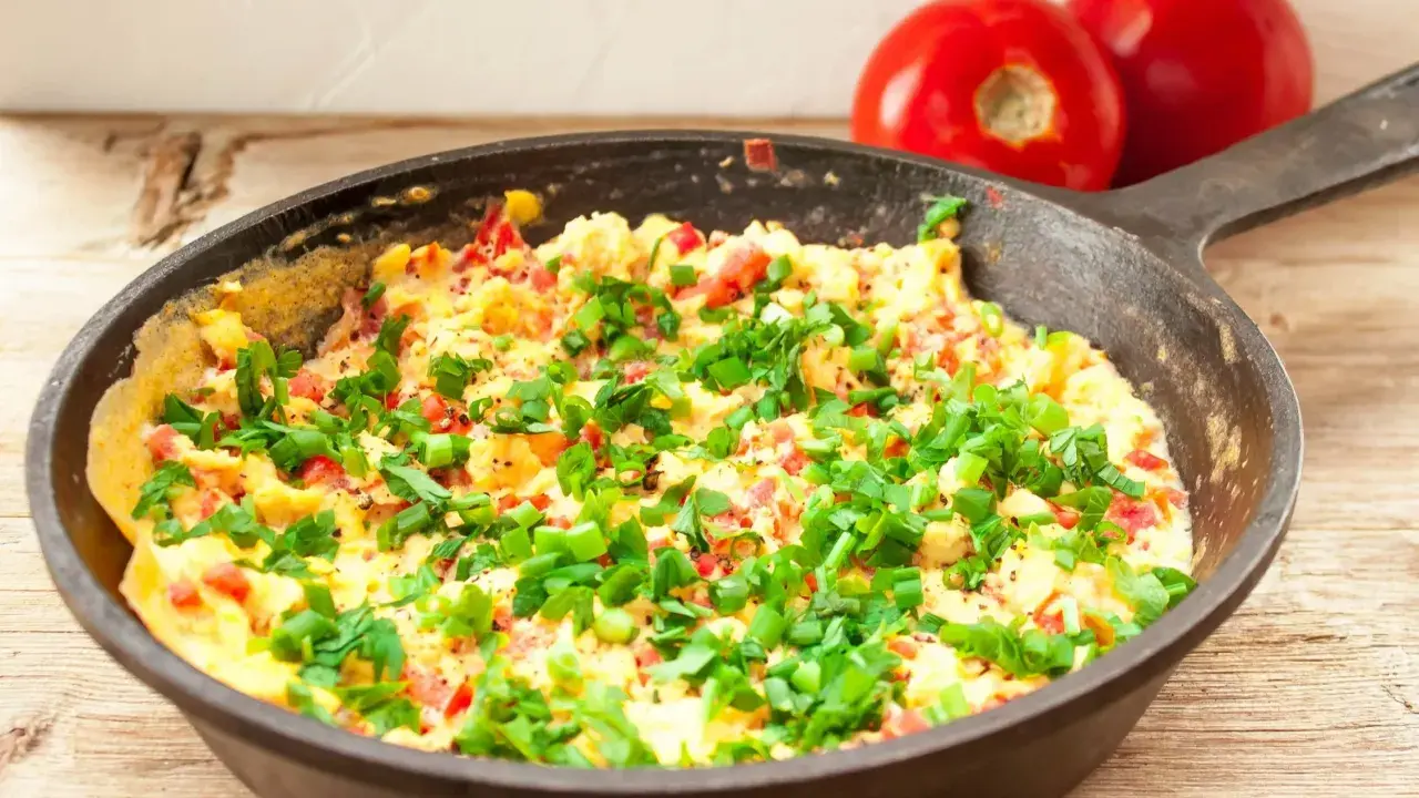 Pyszny omlet z warzywami, posypany szczypiorkiem, gotowy do podania. Obok leżą dwa pomidory.