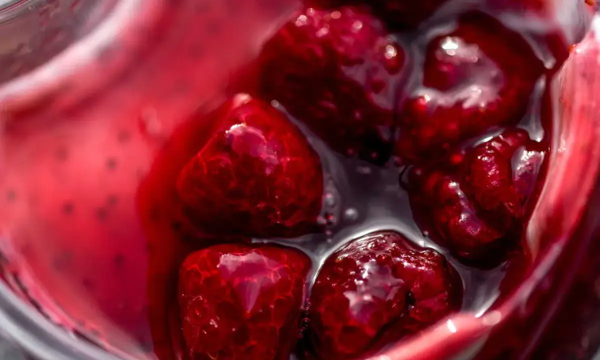 Gros plan sur des framboises dans un liquide rouge vif, parfait pour un nappage framboise facile et gourmand.