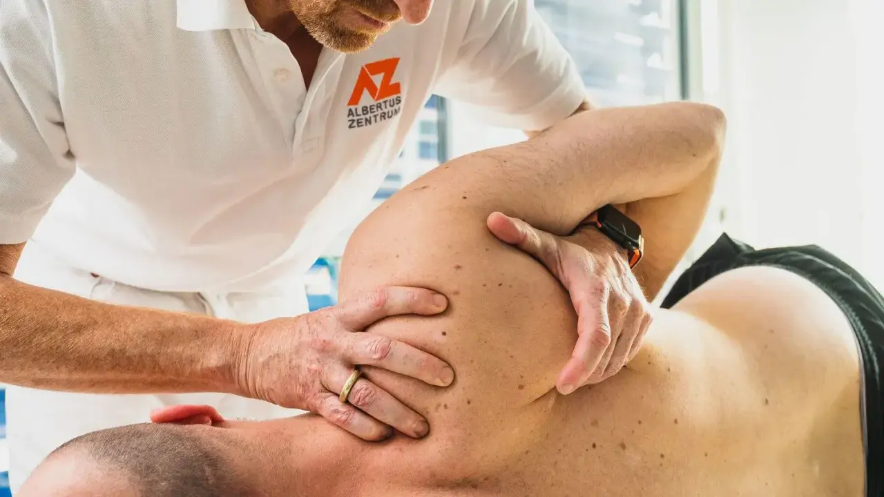 Therapeut führt eine gezielte Massage bei Schulterschmerzen durch. Hände des Therapeuten bearbeiten den Schulterbereich eines liegenden Patienten.