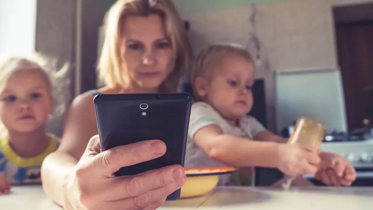 Madre con su móvil, mientras sus hijos pequeños, de unos 2 años, miran pantallas.