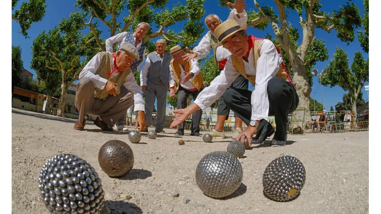 Des hommes jouent à la pétanque sous les platanes. La question "la pétanque est-il un sport ?" se pose devant leur concentration.