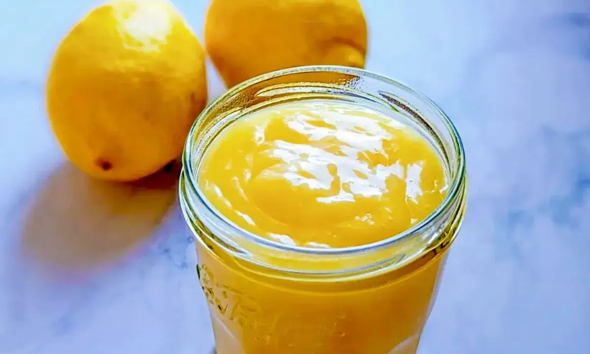 Un pot de lemon curd sans maïzena, onctueux et doré, à côté de deux citrons frais. Parfait pour une touche acidulée.
